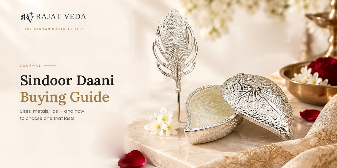 An open German Silver sindoor daani with a filigree lid and a feather-shaped sindoor pin resting on a marble slab