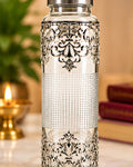 German Silver filigree glass water bottle standing on marble beside a lit diya